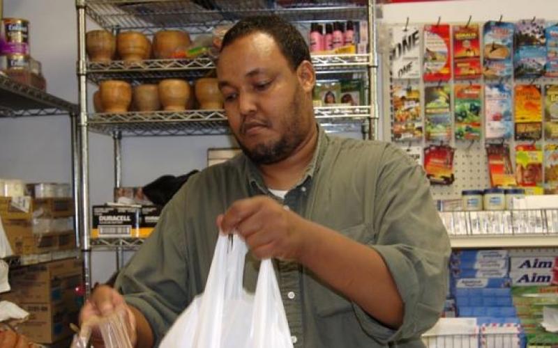 In 2000, Abdiqafar Adan organized seven other partners to start the Afrik grocery store and wholesale operation on Cedar Avenue. Photo of Abdiqafar Adan bagging a customer purchase in his grocery