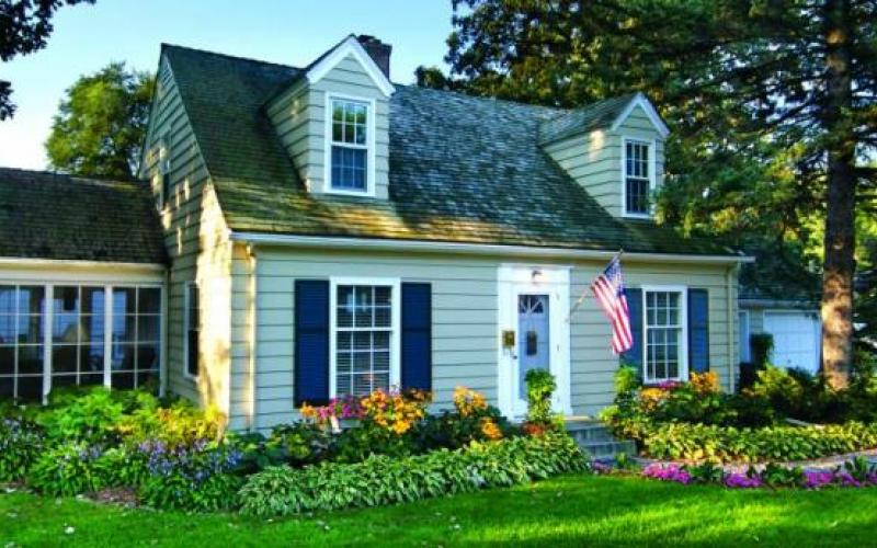 Stock image of a new 1.5-story home with sunroom on side, and lush garden and lawn