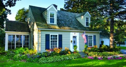 Stock image of a new 1.5-story home with sunroom on side, and lush garden and lawn